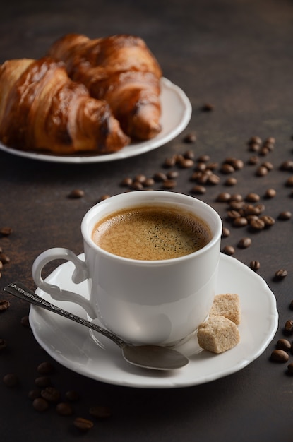 Cup of fresh coffee with croissants on dark.