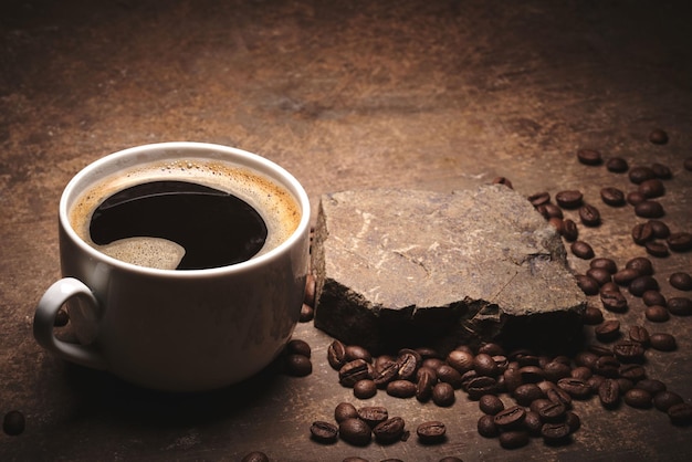 Cup of freshly brewed roasted coffee beans on brown background