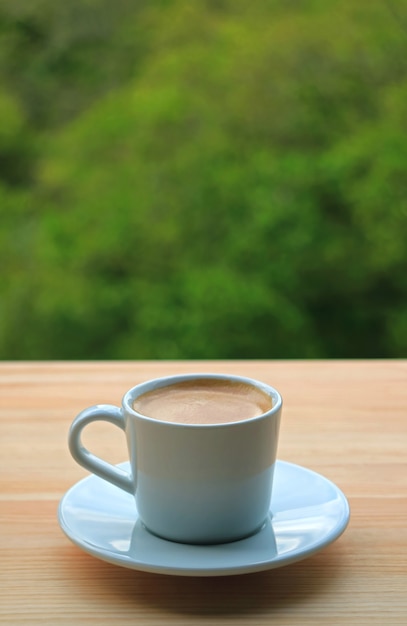 Cup of Frothy Coffee with Blurry Green Foliage in the Backdrop