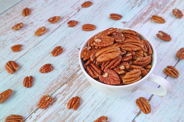 Cup Full of Pecan Nuts with Some Kernels Scattered around on Wooden Table