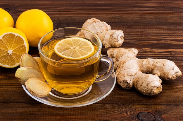 Cup of Ginger tea with lemon, honey and ginger root on a wooden background.