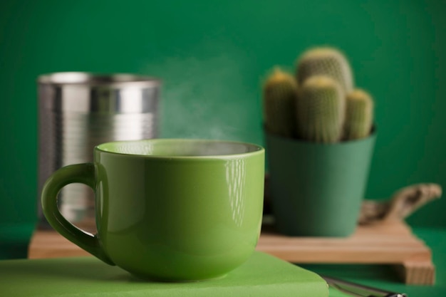 cup of green tea or coffee hot with steam cactus and recycled metal can green background