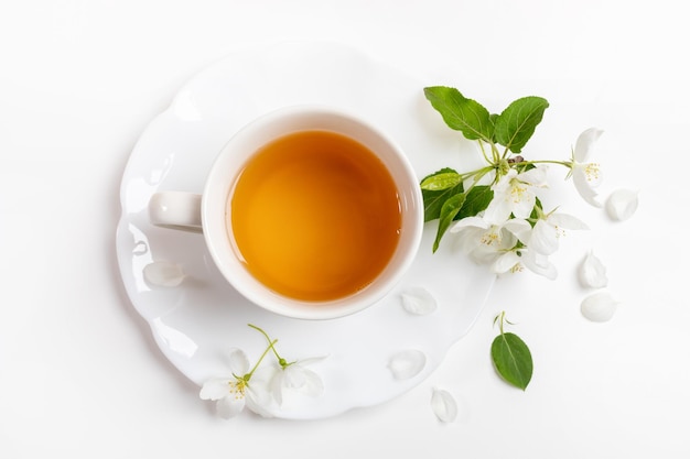 Cup of green tea on figured saucer with white apple tree flowers on white background Top view