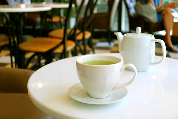 Cup of green tea and teapot on white round table in a tearoom