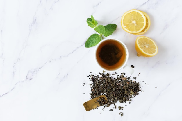 Cup of green tea with lemon and mint top view on white marble background