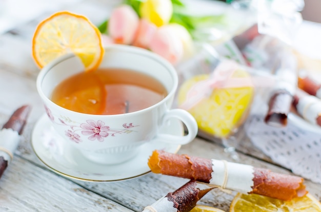 Cup of green tea with lemon slice, dry fruits leather roll and ginger cookies, tulips