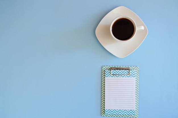 Cup of hot black coffee with notebook paper pen Top view Copy space Flat lay on blue background