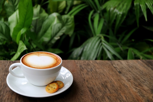 Cup of Hot Cappuccino Coffee with Cookies Served on Wooden Table with Blurry Green Foliage 