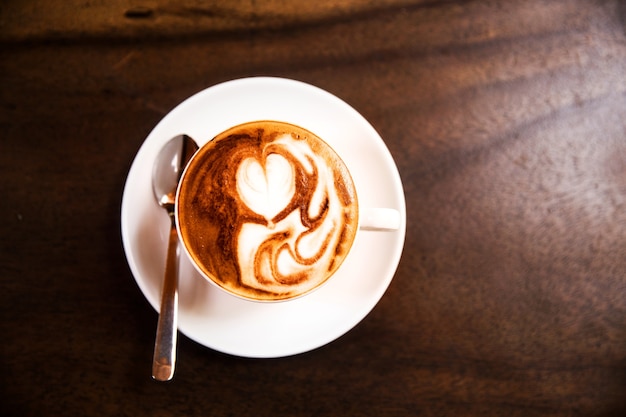 Cup of hot cappucino is on the wooden table. It is an art on the latte.