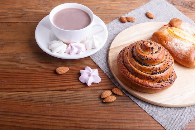 A cup of hot chocolate and buns  on brown wooden surface.