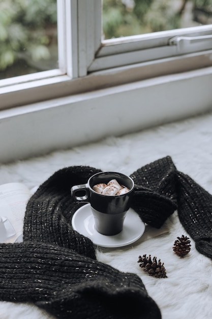 A cup of hot chocolate with marshmallow arrange with knitted warm winter scarf.