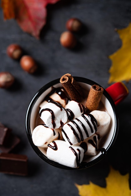 A cup of hot chocolate with marshmallow nuts and cinnamon on a dark gray table Autumn concept