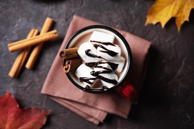 A cup of hot chocolate with marshmallows and cinnamon on a dark brown table Autumn concept of a warming drink Top view