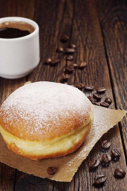 Cup of hot coffee and sweet doughnut on dark wooden table