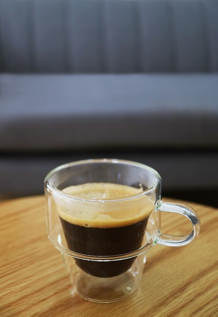 Cup of hot coffee in a transparent cup with blurry couch in background