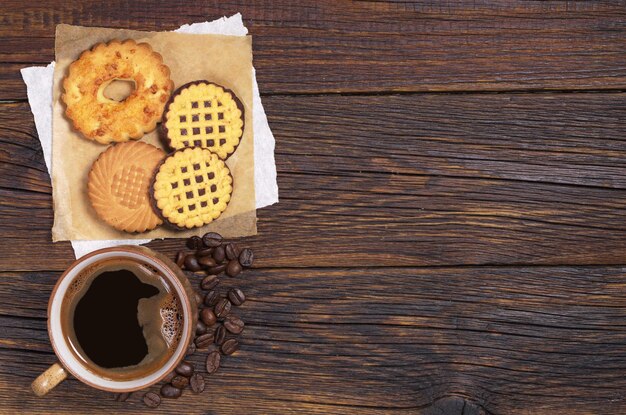 Cup of hot coffee and various cookies on dark wooden table, top view. Space for text