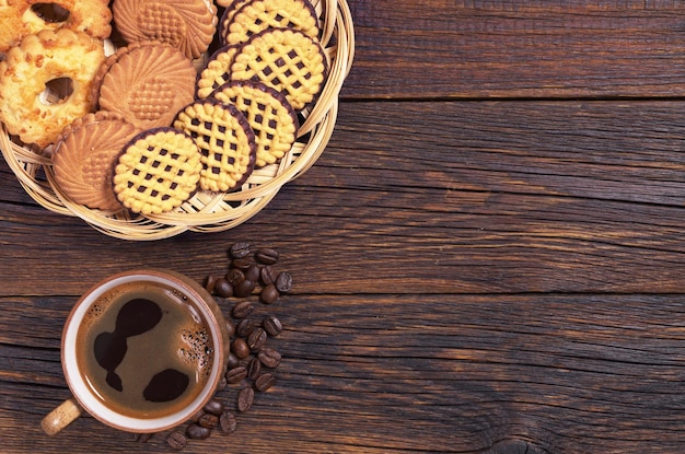 Cup of hot coffee and various cookies in plate on dark wooden table top view Space for text