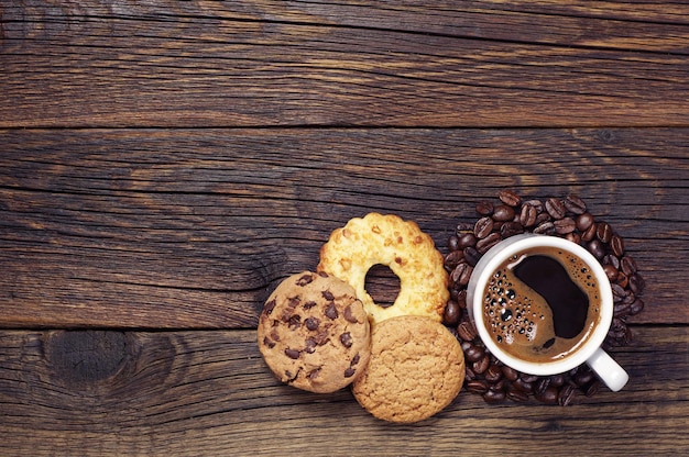 Cup of hot coffee and various sweet cookies on dark wooden table, top view