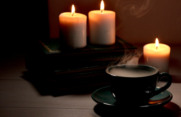 Cup of hot coffee with green  smoke books and burning candles Desk table in power supply cut