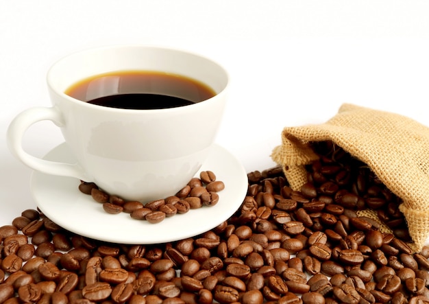 Cup of hot coffee with roasted coffee beans scattered from burlap bag