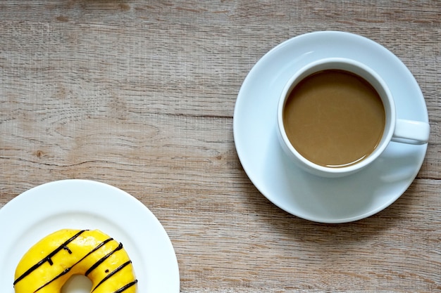 A cup of hot coffee with yellowcolored sweet donuts on wooden background