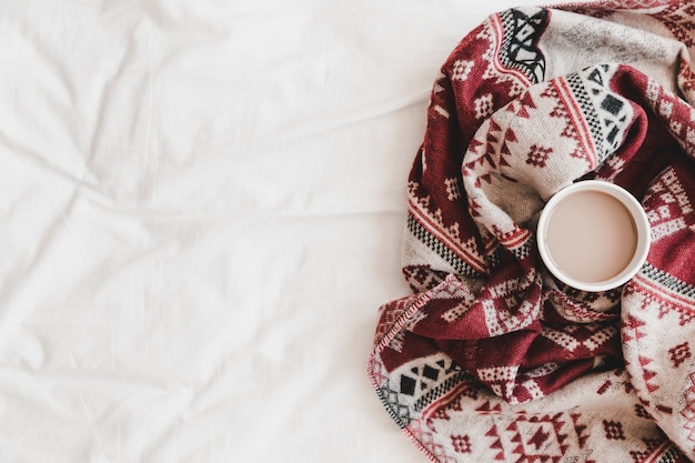 Cup of hot drink in patterned plaid on bedsheet