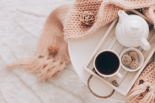 Cup of hot drink and teapot on a serving tray, knitting clothes.