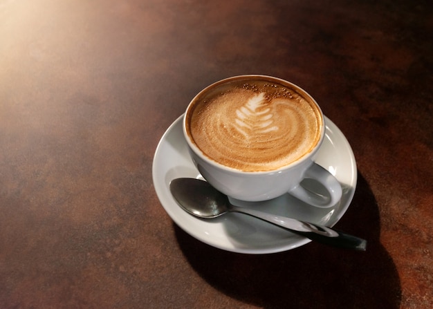 Cup of hot latte art in afternoon light on wooden table 