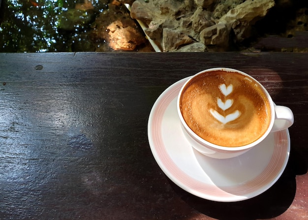 A cup of hot latte art coffee on a wooden table in the garden.