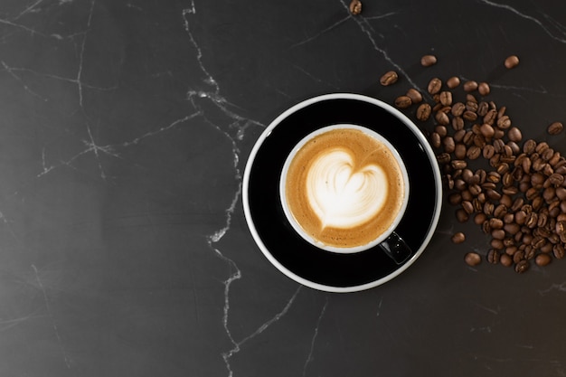 Cup of hot latte coffee with beautiful milk foam latte art texture with coffee bean on black marble background. Overhead view, copy space. Advertising for cafe menu. Coffee shop menu.