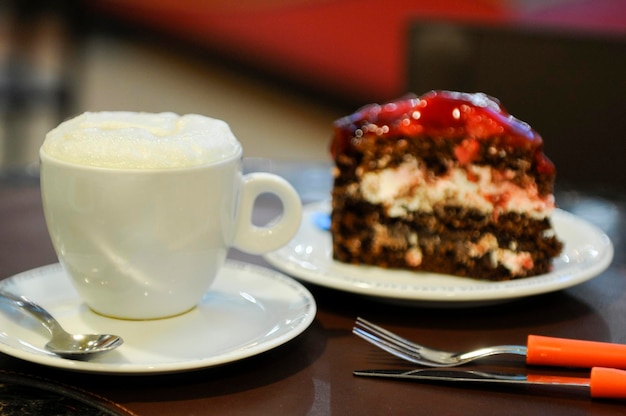 Cup of hot milk on a coffee shop table with a slice of strawberry chocolate tart  blurred background