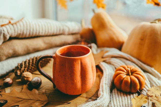 A cup of hot steaming tea and a pumpkinshaped candle on the windowsill autumn mood