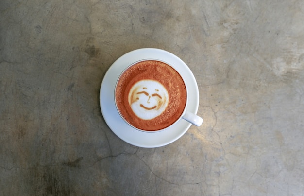 Cup of hot tasty cappucino with smile as art latt onn concrete background