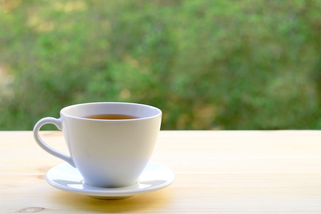 Cup of hot tea isolated on outdoor table with blurry foliage in background