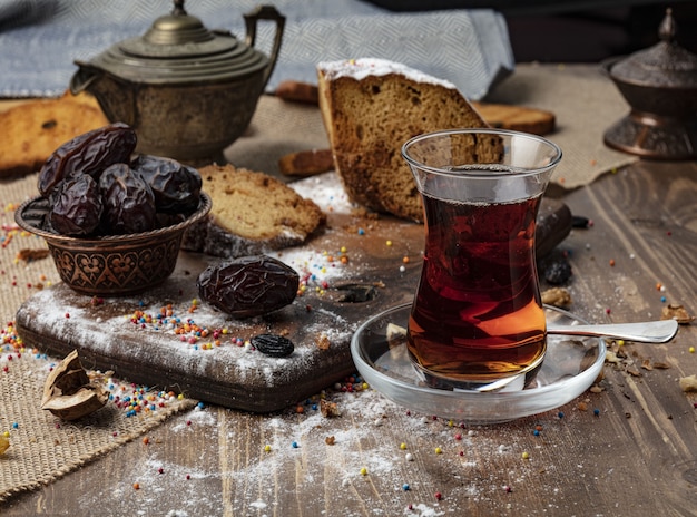 A cup of hot tea with dates on wooden background.