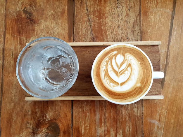 A cup of latte art coffee with drinking water on wooden background.