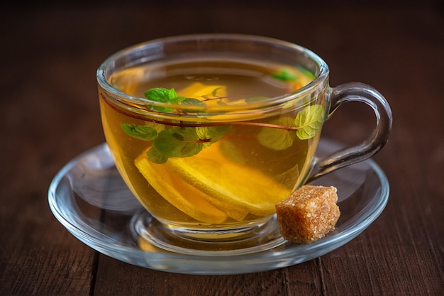 Cup of Lemon tea with lemon slices, cane sugar and mint on dark wood.