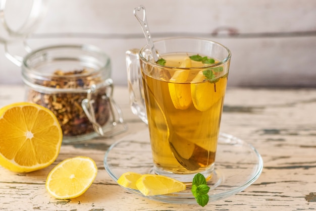 Cup of Lemon tea with lemon slices and mint on light wooden table.