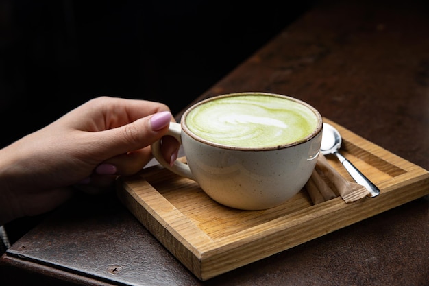 A cup of matcha latte with a spoon on a wooden tray