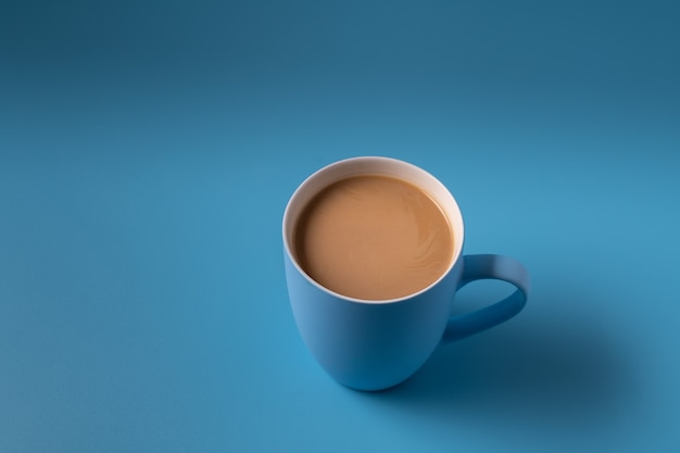 Cup of milk coffee on blue background, copy space for text.