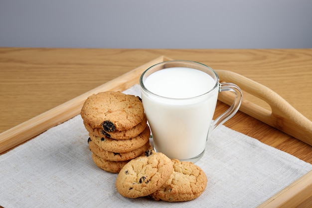 Cup of milk and cookies with raisins on a wooden tray