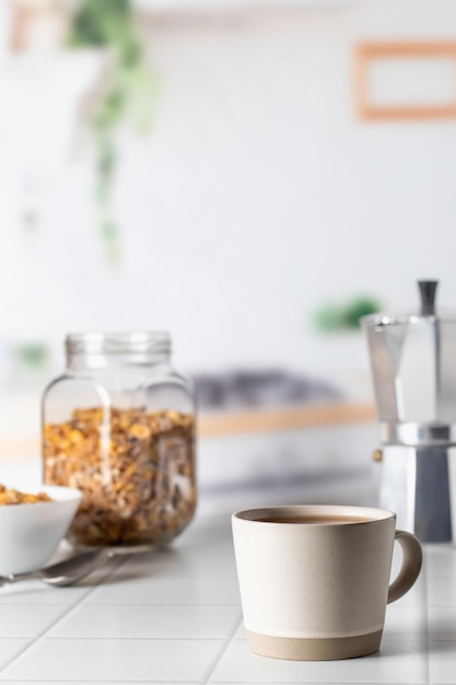 Cup of morning coffee on white tile tabletop in kitchen Healthy breakfast consept with coffee and muesli Text space