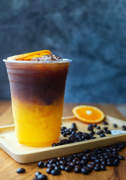 A cup of orange and black iced coffee sits on a tray next to a pile of coffee beans.