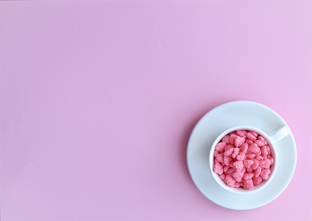 A cup of pink candy sits on a pink background with a white plate that says'love'on it.