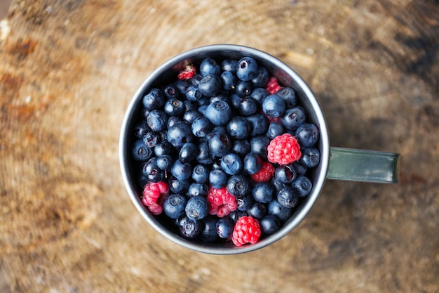 Cup of raspberries and blueberries on the wooden background