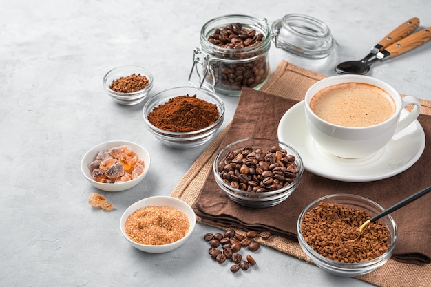 A cup of refreshing coffee on a gray wall with different types of coffee. Side view, copy space.