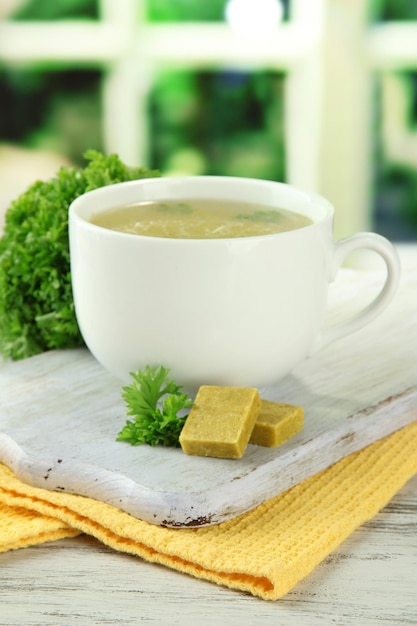 Cup of soup with bouillon cubes on wooden table