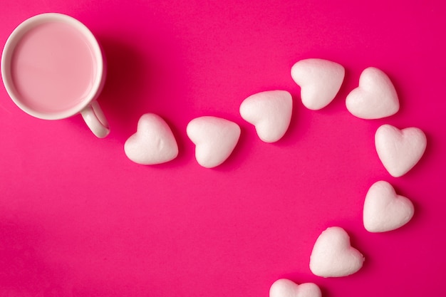 Cup of strawberry milk with heart shape symbol on pink.