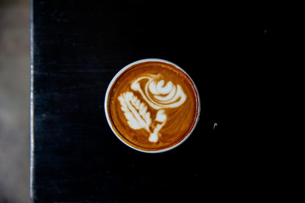 Cup of tasty cappuccino with latte art on black table background