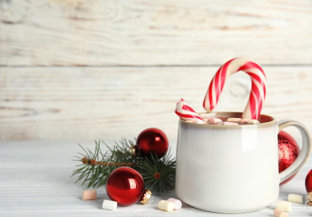 Cup of tasty cocoa with marshmallows candy cane and Christmas decor on white wooden table Space for text